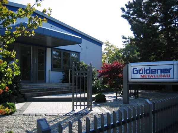 Eingangsbereich eines modernen Metallbau-Unternehmens mit Firmenlogo und Garten.