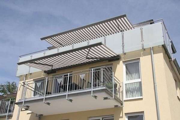Moderne Balkonüberdachung mit Glas und Markise an einem Mehrfamilienhaus im Sonnenschein.
