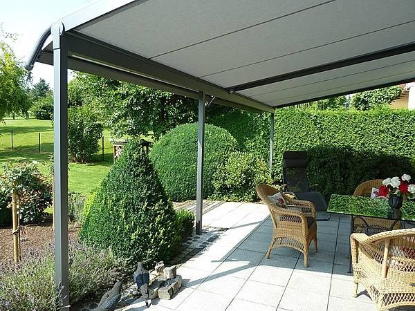 Überdachte Terrasse mit Gartenmöbeln und Blick auf gepflegten, grünen Garten.