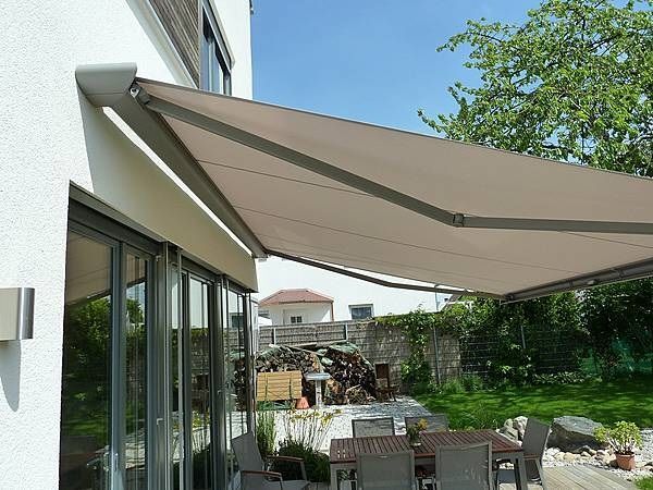 Moderne Terrassenüberdachung mit Markise am Haus, Gartenmöbel und grüner Garten im Sommer.