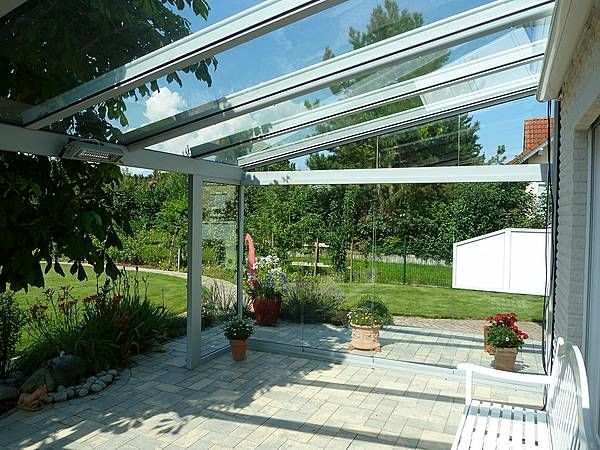 Moderne Terrassenüberdachung aus Glas mit Gartenblick und bepflanzten Blumentöpfen.