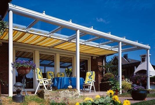Überdachte Terrasse mit Markise und Gartenmöbeln vor einem Einfamilienhaus im Sommer.