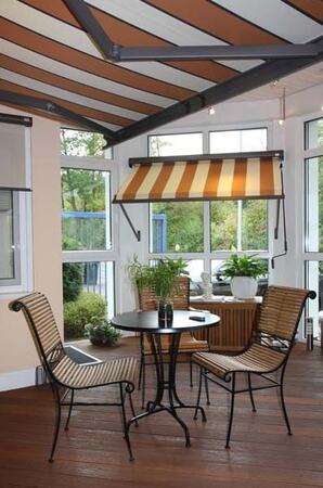 Gemütlicher Wintergarten mit Markise, Holzboden, Tisch, Stühlen und vielen Pflanzen.