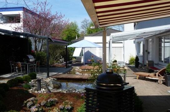 Moderner Garten mit Terrasse, Grillplatz, Teich, Blumenbeet und Sonnenschutz-Markisen.